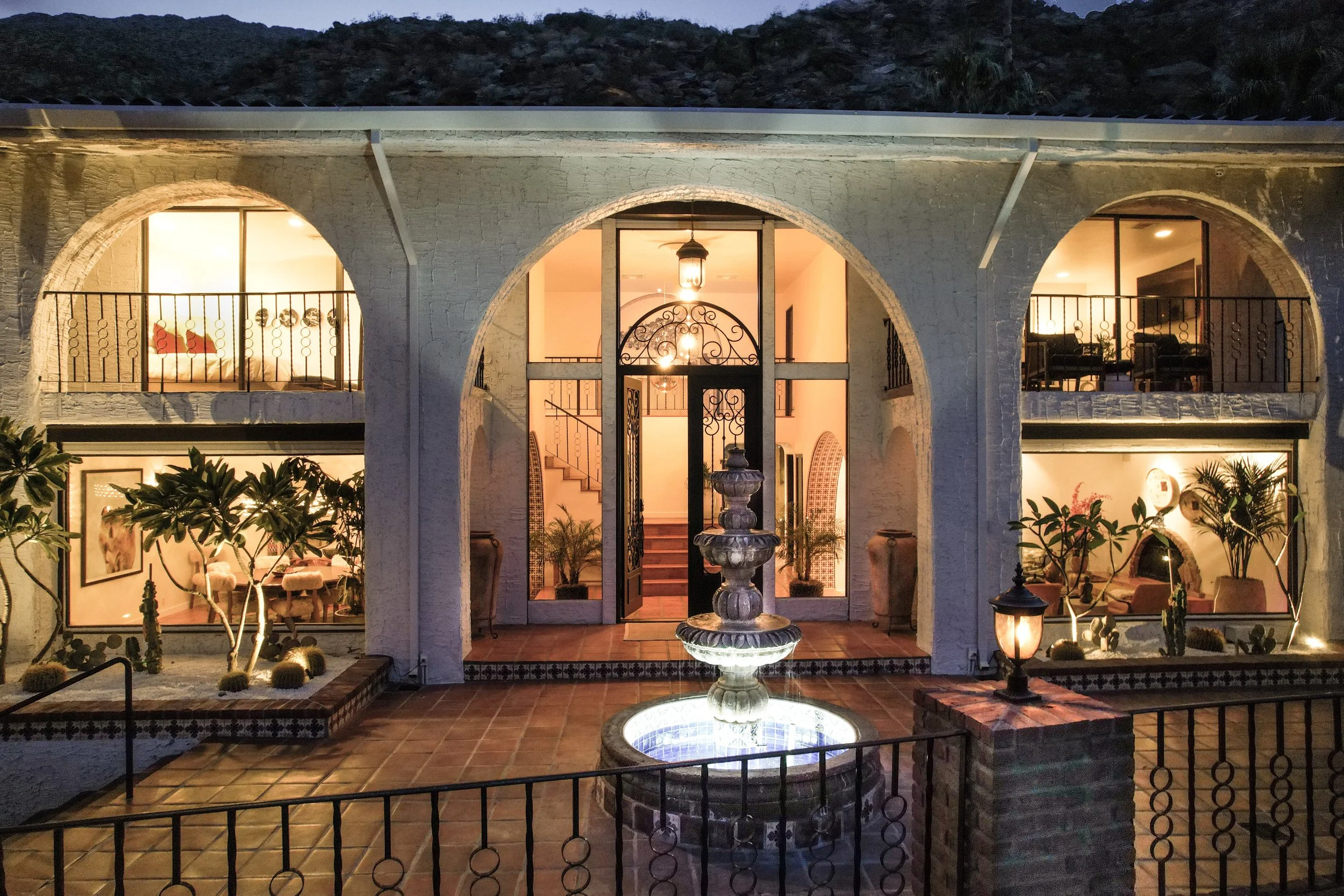 The arched front elevation of Ridge House lit at dusk, with a tiled courtyard and stone fountain.