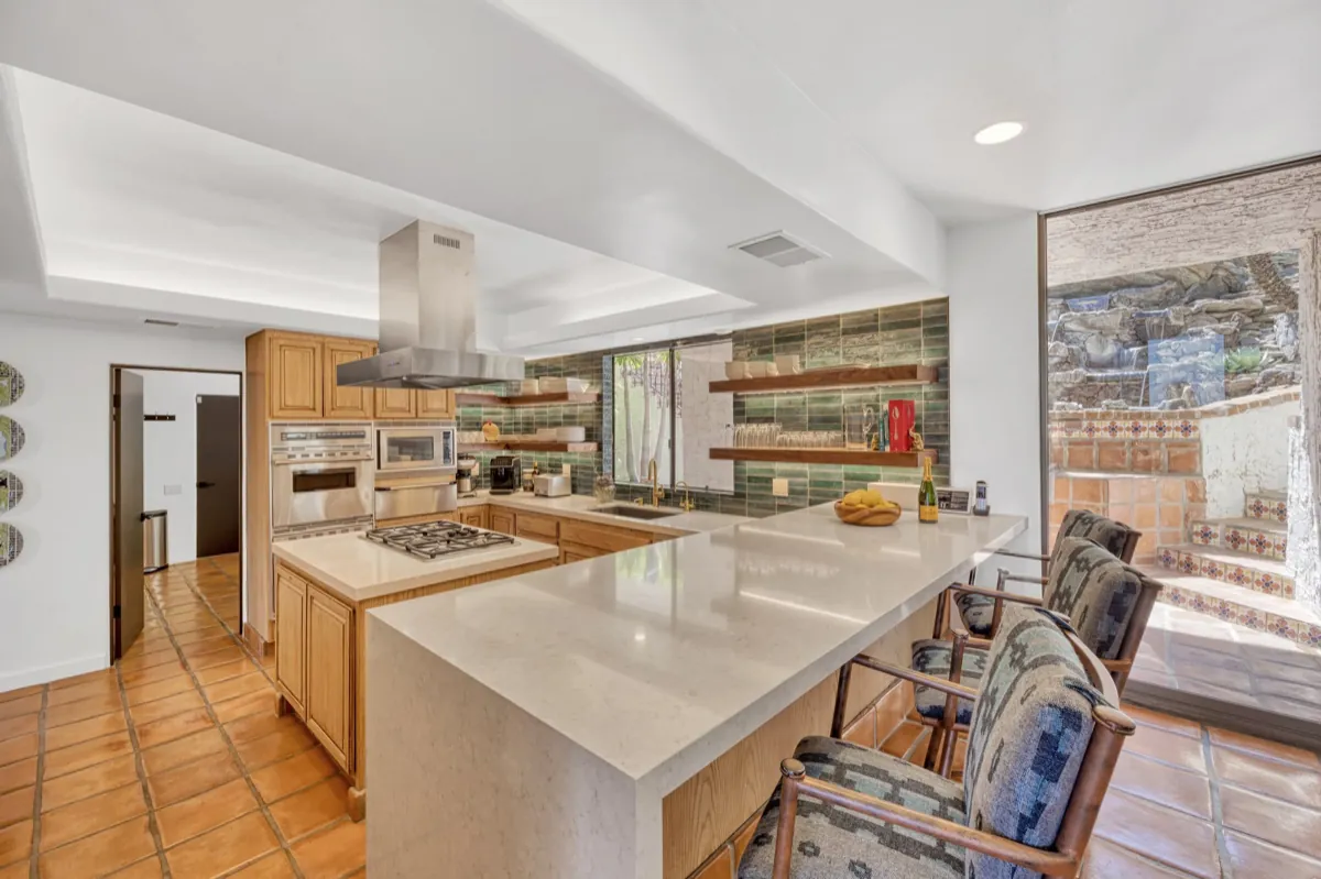 Kitchen with a long stone island, stainless range hood and open walnut shelving.