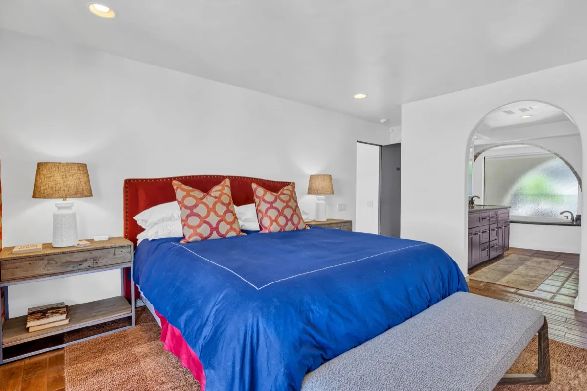 The Ridge Suite, with a red upholstered headboard, blue linens and an arched doorway to the bath.