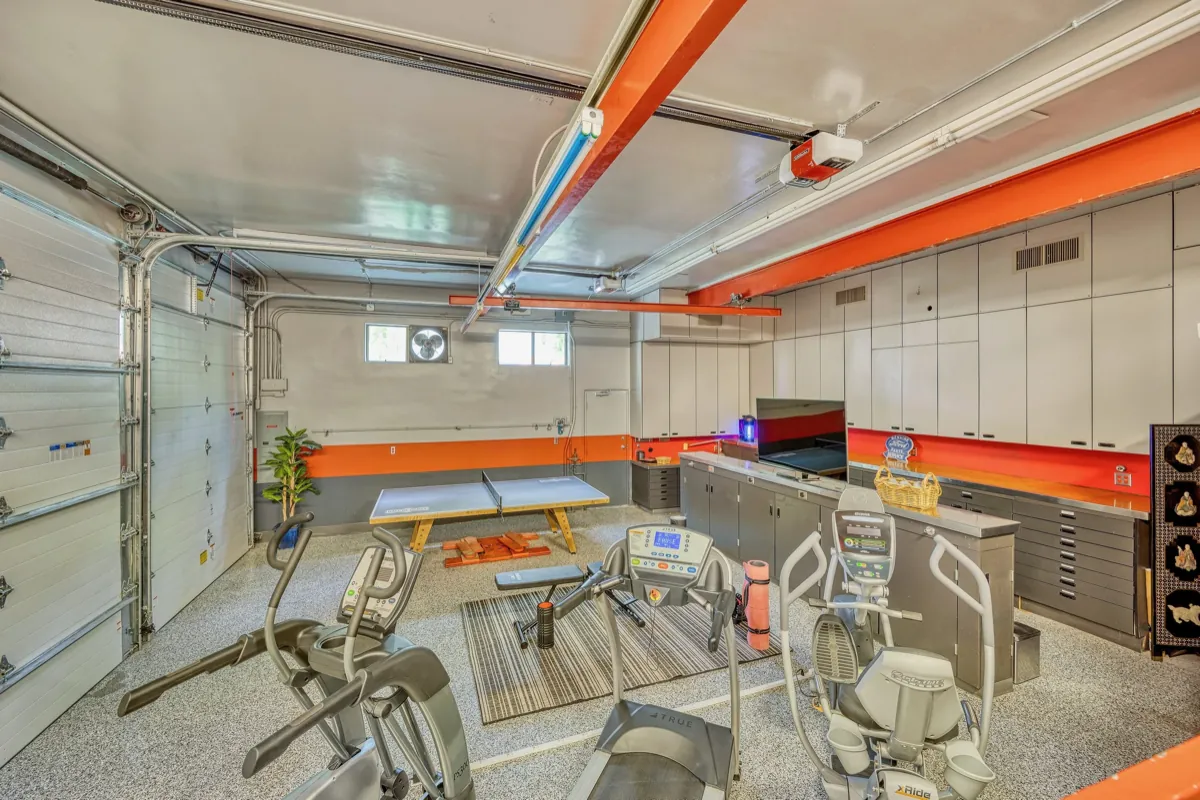 The home gym, with cardio equipment, storage cabinetry and a glass garage door.