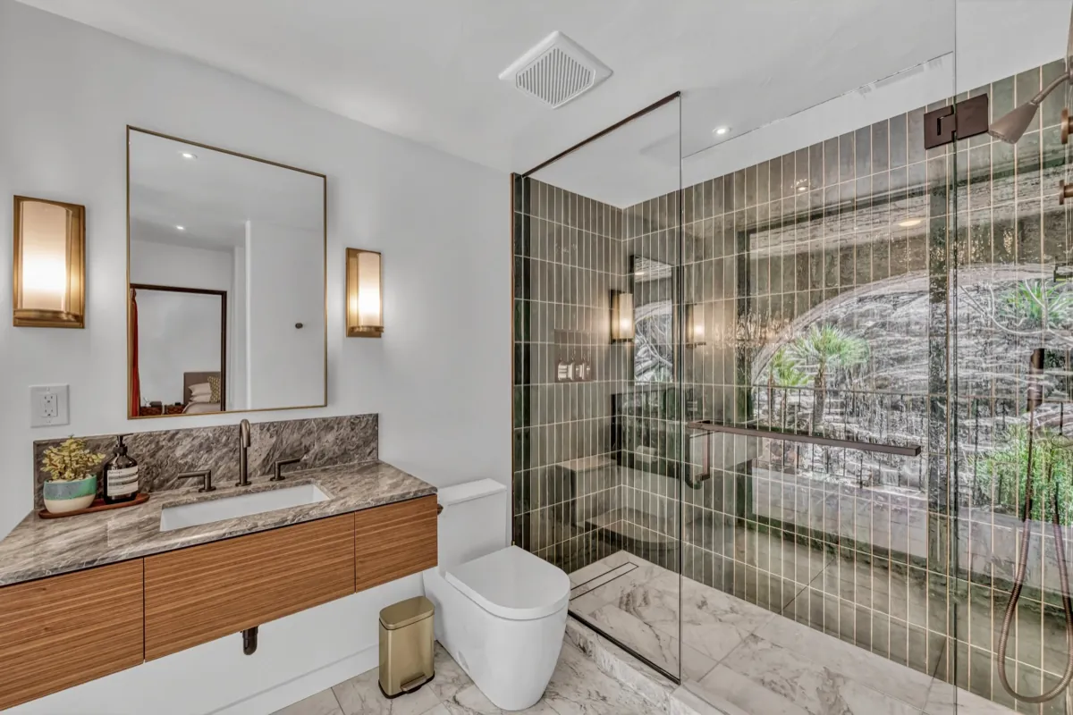 Walk-in glass shower with a floating walnut vanity and marble counter.