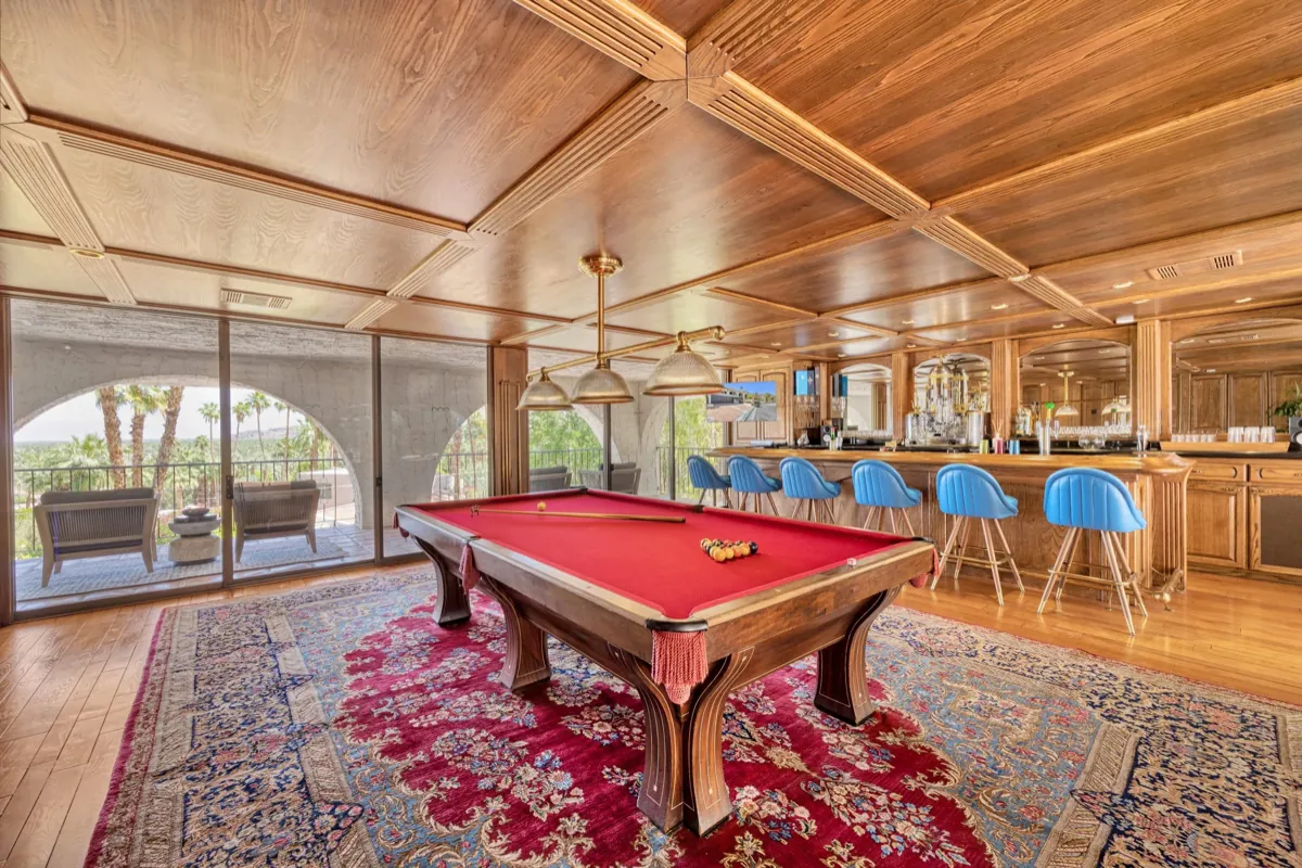 Wood-panelled saloon with a red billiards table, blue bar stools and a patterned rug.