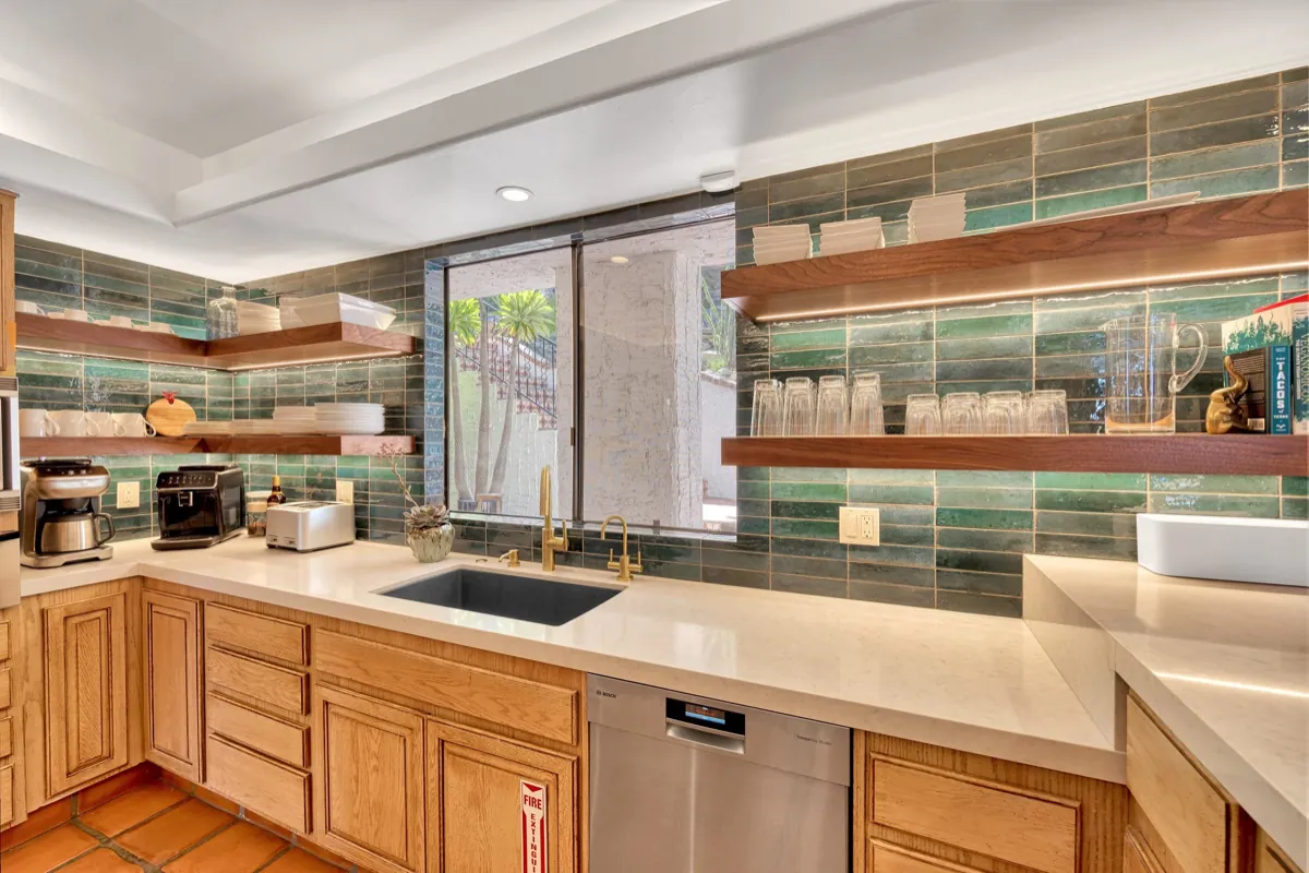 Kitchen counter run with a green tile backsplash, walnut shelves and brass fittings.