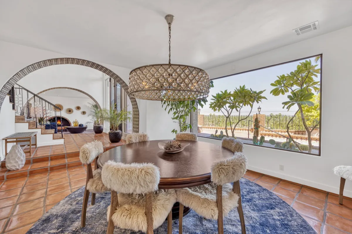 Dining room with a round wood table, sheepskin-draped chairs and a wide window onto the palms.