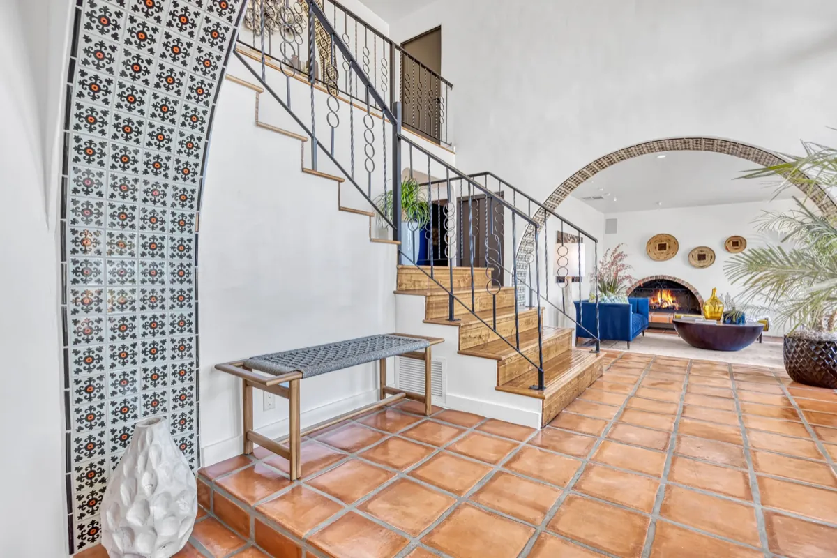 Entry hall with a mosaic-tiled arch, ironwork stair rail and terracotta tile leading into the living room.